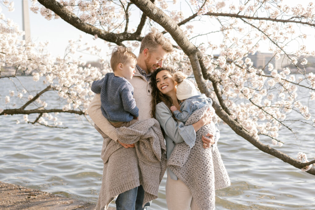 Mom and dad with two children under cherry blossoms in Washington, DC.