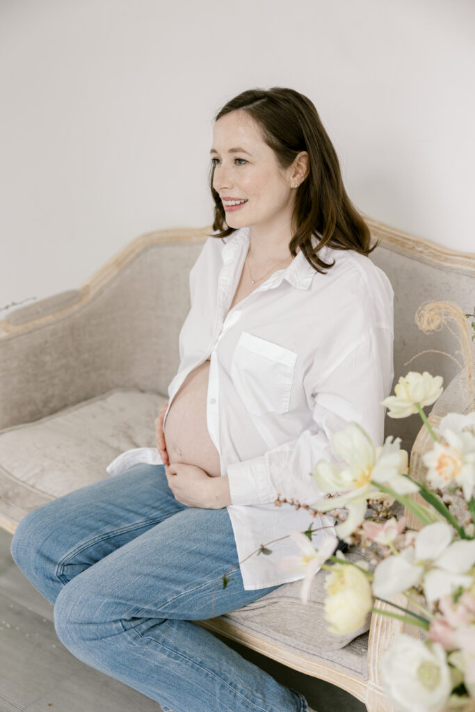 Woman sitting on a bench surrounded by flowers holding her pregnant belly during a Northern Virginia motherhood session