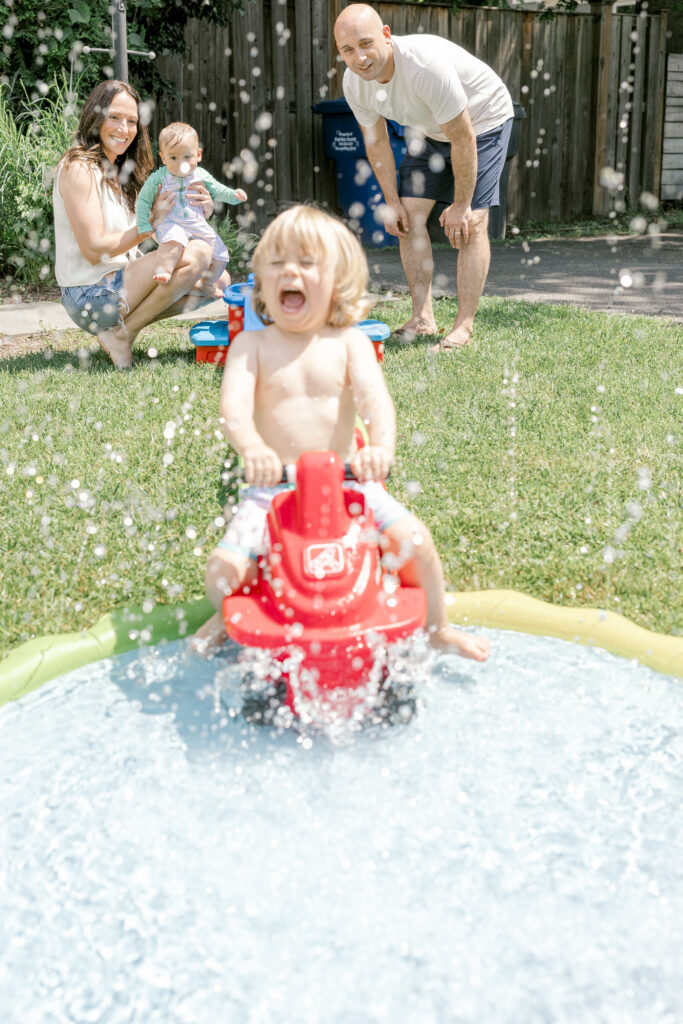 Kids running through a lawn sprinkler, highlighting playful summer family photo ideas in Northern Virginia.