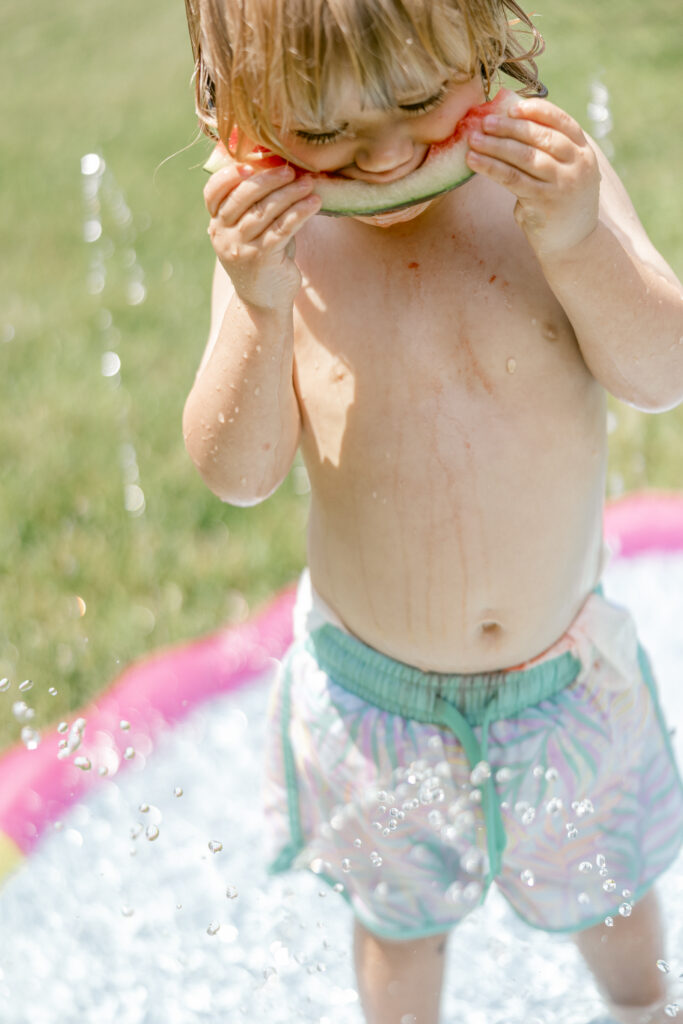 Toddler eating watermelon during a fun, backyard summer family portrait session.