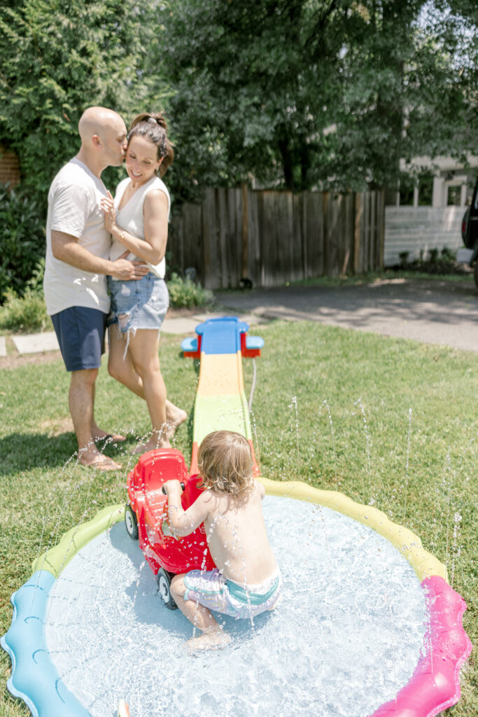 Candid family photography of a boy playing in water while his parents watch.