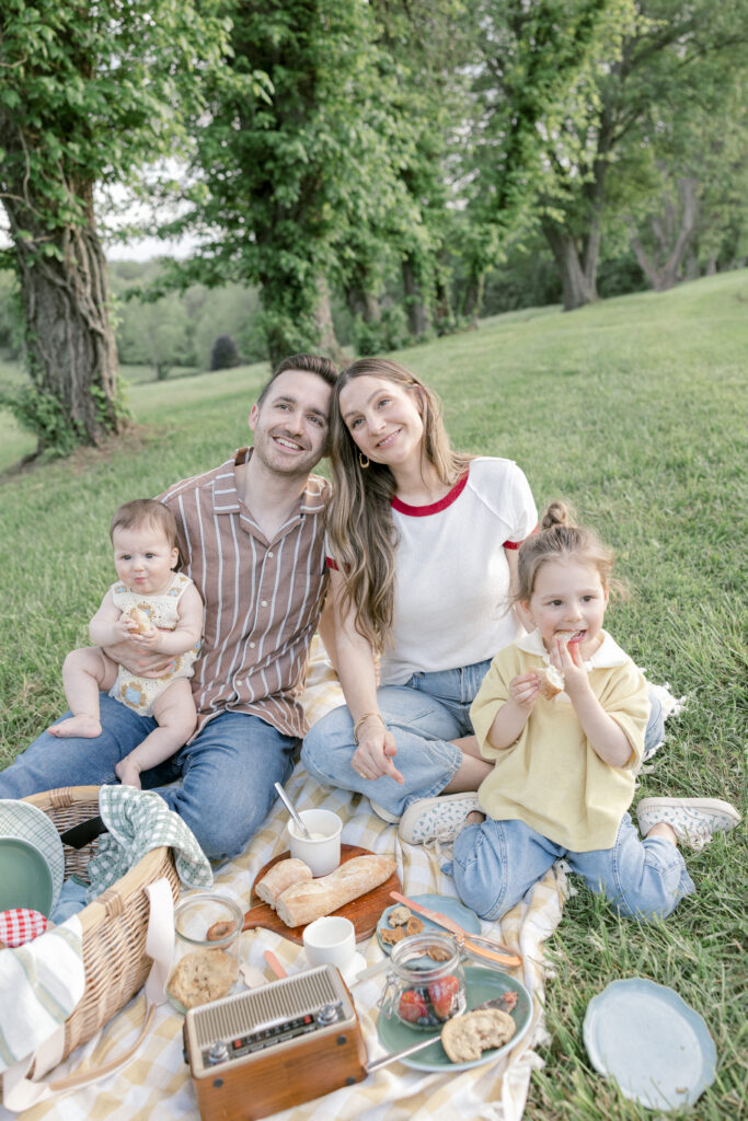 A family cuddling on a picnic blanket under a shade tree, one of the best summer family photo ideas in Northern Virginia.