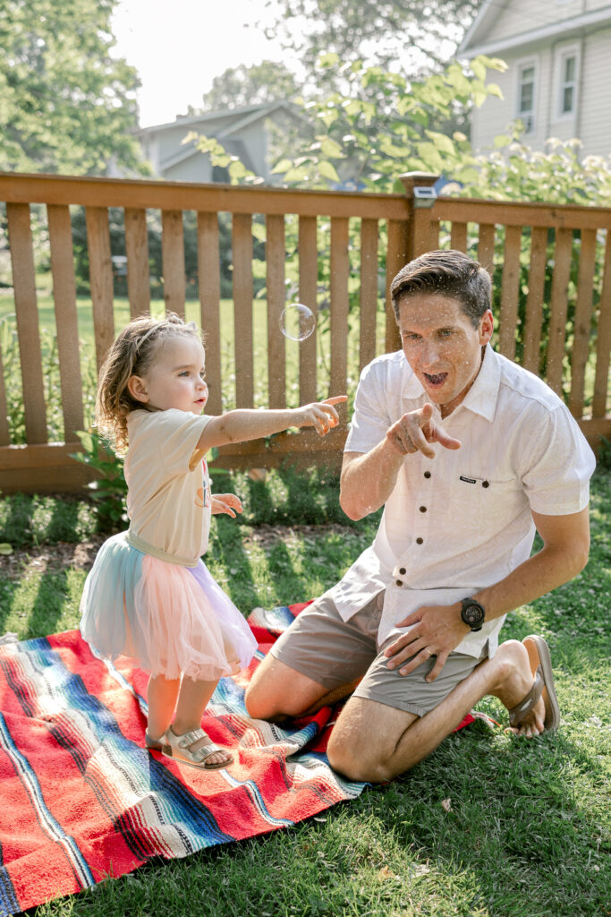 Toddler and dad popping bubbles during a playful backyard family photo session.