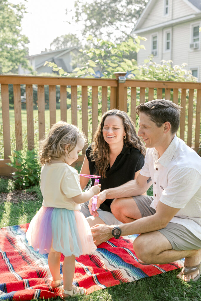 A mom and dad laughing while blowing bubbles for their daughter during a relaxed lifestyle photography session.