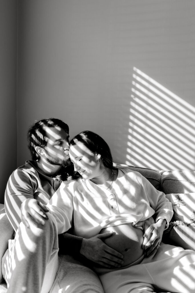 Man kissing pregnant woman's forehead in their home photography session.