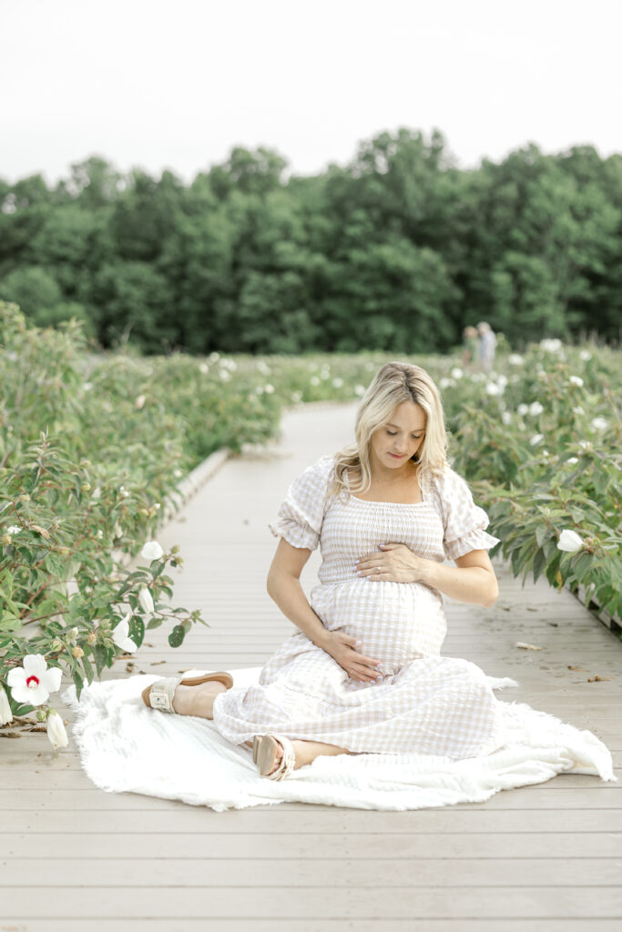 Pregnant woman on a boardwalk surrounded by greenery and flowers in Northern Virginia.
