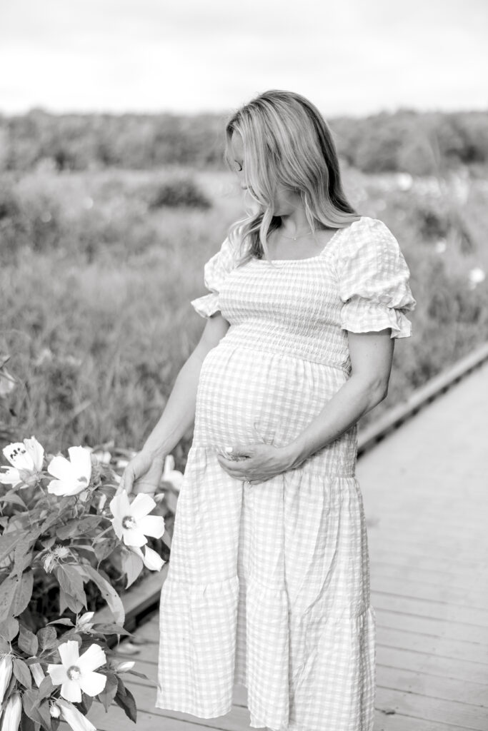A black and white image of a pregnant woman gently touching a flower in Northern Virginia.
