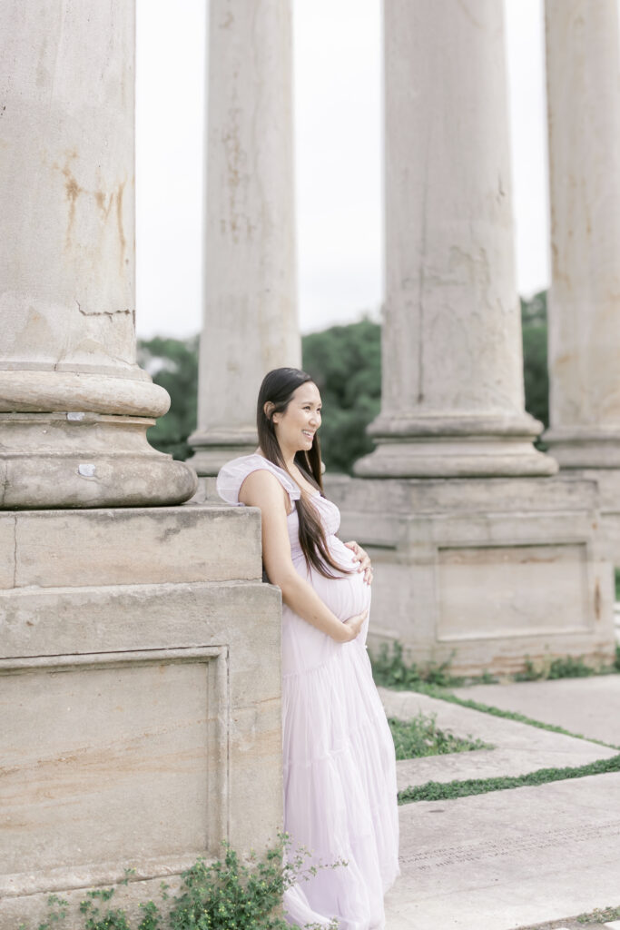 Pregnant woman leaning against a column smiling into the distance in Washington DC