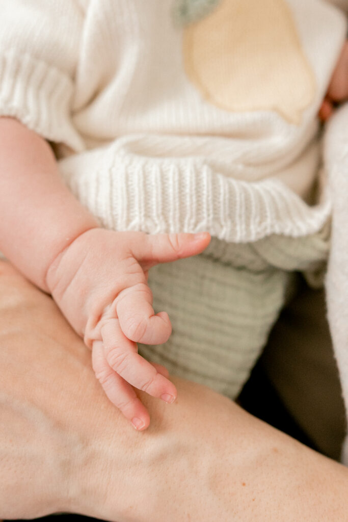 Close-up of a newborn baby’s tiny hand gently resting in a parent’s hand during the early postpartum days.